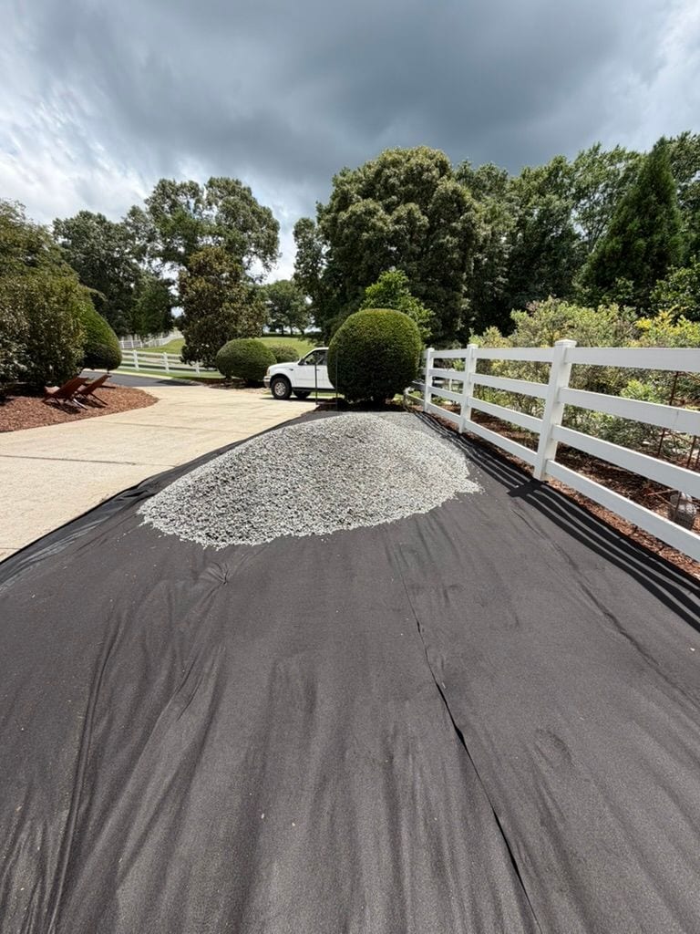 Ground cloth laid and a pile of gravel waiting, fence line behind