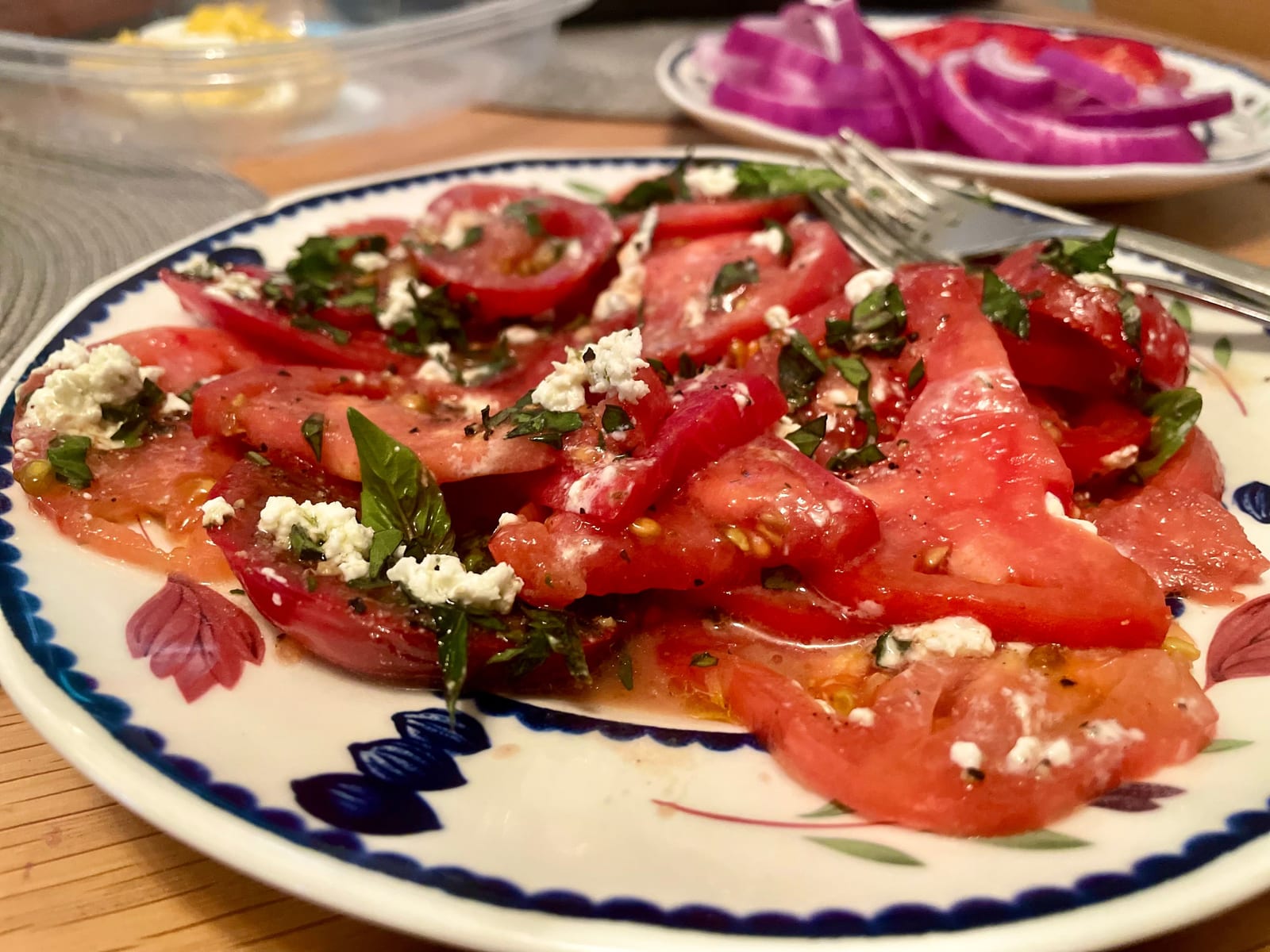 The finished dish on a blue-rimmed plate: sliced tomato, torn basil, crumbled cheese and a balsamic drizzle